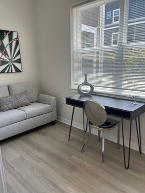 South Brunswick apartment for rent - A room with a grey couch, a table with a chair and a dartboard on the wall.