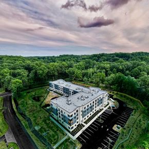 Princeton apartment for rent - A large white building with a grey roof is surrounded by a parking lot and greenery.