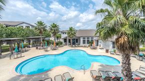 Conroe apartment for rent - A large outdoor swimming pool surrounded by lounge chairs and palm trees at Rosemary Apartments, Conroe, TX, 77384
