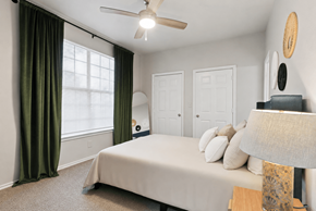San Antonio apartment for rent - A bedroom with a bed, a ceiling fan, and a window with green curtains.