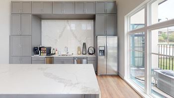A kitchen with gray cabinets and a marble counter top