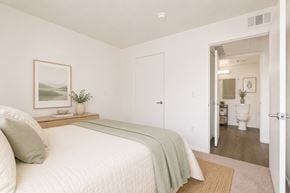 Huntington Park apartment for rent - A bedroom with a bed, a nightstand with a plant, and a painting on the wall.