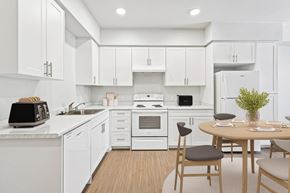 La Mesa apartment for rent - A modern kitchen with white cabinets and appliances, a wooden table with chairs, and a plant on the table.