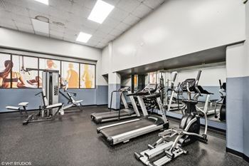 A gym with treadmills and other exercise equipment in a building with windows