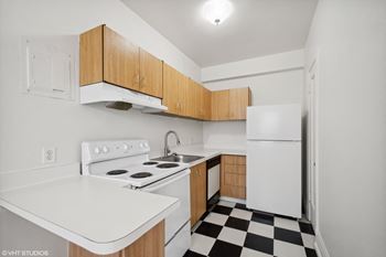 A kitchen with white appliances and wooden cabinets and a checkered floor
