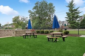 Two picnic tables on the grass in front of a patio with umbrellas