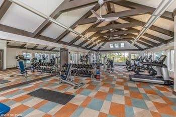 A gym with weights and cardio equipment in a building with windows