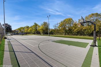A basketball court with a green and grey surface and a basketball hoop on the right side.