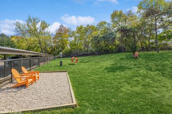 A fenced in dog park with a gravel area and orange chairs