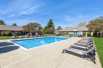 A large swimming pool surrounded by lounge chairs and houses in the background.