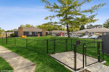 A fenced in dog park in a yard with a tree