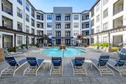 Memphis apartment for rent - an outdoor pool with blue chairs and umbrellas in front of an apartment building at Bristol On Union Apartment Homes, Memphis, 38104