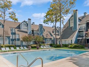 Houston apartment for rent - A swimming pool in front of a large building with a tree in the background.