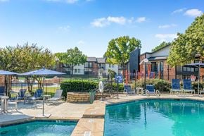 Irving apartment for rent - A swimming pool surrounded by lounge chairs and umbrellas with a building in the background at Water Ridge Apartments , Irving, TX