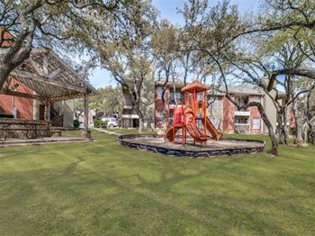 A playground with a red slide in the middle of a grassy area.