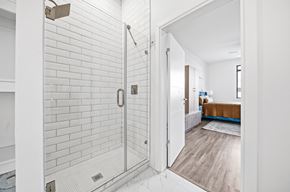 Dayton apartment for rent - A white tiled bathroom with a walk-in shower and a wooden floor leading to a bedroom.