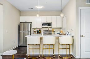 Sunbury apartment for rent - a kitchen with white cabinets and a bar with three stools