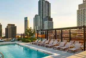 Long Island City apartment for rent - A pool with chairs and a sign that says "SPECTACULAR VIEWS" in front of a city skyline.