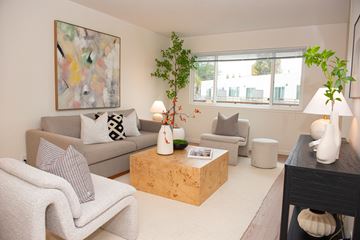 San Jose apartment for rent - A living room with a grey couch, a white chair, a wooden coffee table, and a painting on the wall.