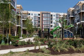 Silver Spring apartment for rent - A playground with a green slide and a white swing set is surrounded by a garden with red flowers and green shrubs.