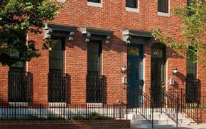 Baltimore apartment for rent - A red brick building with a green door and black iron fencing.