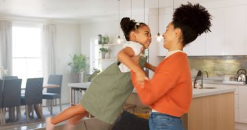 Arlington apartment for rent - A woman in an orange top is holding a child in a green dress in a kitchen.