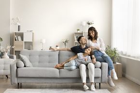 Arlington apartment for rent - A woman and a child are sitting on a grey couch with a man lying on the floor.