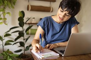 Arlington apartment for rent - A person in a blue shirt is writing in a notebook with a laptop open beside them.