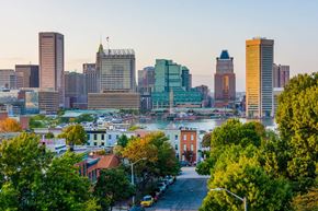 Baltimore apartment for rent - A cityscape with a mix of modern and older buildings, a river in the middle, and a tree-lined street in the foreground.
