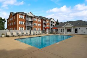 Madison apartment for rent - A large swimming pool is surrounded by lounge chairs in front of a red brick apartment building.