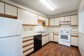 Grand Forks apartment for rent - A white refrigerator is in a kitchen with wooden floors and white cabinets.