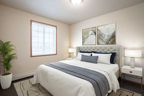 Fargo apartment for rent - A bedroom with a large bed, a potted plant, and two framed pictures on the wall.