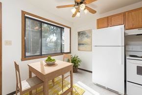 Bismarck apartment for rent - Bismarck, ND Riverpark Apartments a kitchen with white appliances and a wooden table with a bowl of fruit on it. The natural light from the window next to the table brightens the room