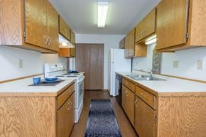 Fargo apartment for rent - a kitchen with wood cabinets and white appliances and a blue rug. Fargo, ND Park Circle Apartments.