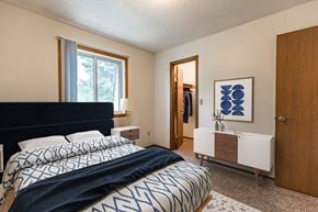 Bismarck apartment for rent - Bismarck, ND Brandon Apartments  a bedroom with a large bed, a blue and white comforter, a large window, and walk-in closet.