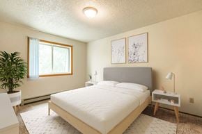 Bismarck apartment for rent - Bismarck, ND Brandon Apartments. The room showcases a comfortable bed with neatly arranged bedding and a calm ambiance. Soft lighting adds to the peaceful atmosphere, while a window allows natural light to fill the space. It's a tranquil retreat for rest and relaxation.
