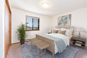 Bismarck apartment for rent - Bismarck, ND Fairview Apartments. A bedroom that showcases a comfortable bed with neatly arranged bedding, a stylish bed bench, and a window that fills the space with natural light. It's a serene and inviting setting for rest and relaxation.