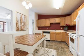 Bismarck apartment for rent - Bismarck, ND Fairview. A Kitchen that showcases appliances, a dining table with chairs, and a bold red accent wall. It's a stylish and inviting area for cooking and enjoying meals.