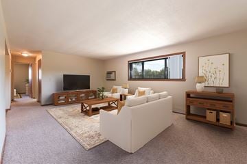 Bismarck apartment for rent - Bismarck, ND Parkview Arms Apartments. A living room with a set of white furniture containing a couch and chairs facing the tv. A large window floods the room with natural light.
