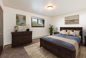 Bismarck apartment for rent - Bismarck, ND Rosser Apartments. A bedroom with dark wood bed, dresser, and night stands. A small window fills the room with natural light
