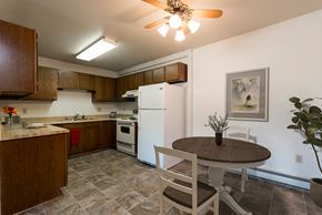 Bismarck apartment for rent - Bismarck, ND Rosser Apartments. A dining room with a table and two chairs. The overhead fan and light brighten the room. A kitchen with a white refrigerator freezer next to a white stove top oven are in the background