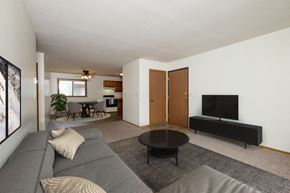 Fargo apartment for rent - Fargo, ND Gemstone Apartments. A living room with a gray couch and a black coffee table. The dining room is in the background with a 4 chair table.