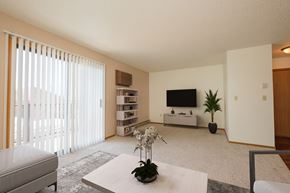 Fargo apartment for rent - Fargo, ND Hunters Run Apartments. A living room with a tv, coffee table, and bookshelf with a large sliding glass door that brightens up the room with natural light.