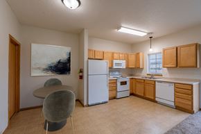 Moorhead townhouse for rent - a kitchen with white appliances and wooden cabinets and a table. Moorhead, MN Townhomes at Mallard Creek