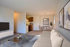 Fargo apartment for rent - A living room with a couch, coffee table, tv, and a dining room in the background. Fargo, ND Place One Apartments.