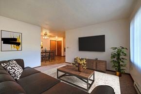 Fargo apartment for rent - Fargo, ND Prairiewood Courts Apartments.  A living room with a couch, coffee table, and a tv. the dining room is in the background.