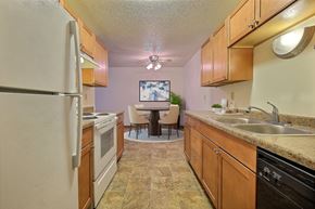 Fargo apartment for rent - a kitchen with wooden cabinets and a dining room in the background. Fargo, ND Village West Apartments