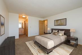 Fargo apartment for rent - Fargo, ND Windgate Apartments. a master bedroom with a large bed and dresser. A bathroom is in the background