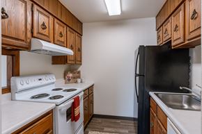 Grand Forks apartment for rent - a kitchen with white appliances and wooden cabinets and a black refrigerator. Grand Forks, ND Cedarwood Apartments