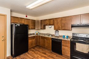 Grand Forks apartment for rent - Grand Forks, ND Stanford Court Apartments. A kitchen with black appliances and a living room in the background a kitchen with wooden cabinets and black appliances